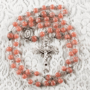 A Rosary with Rhodochrosite Beads and Silver Cross (metal chain) displayed on a white lace fabric background.
